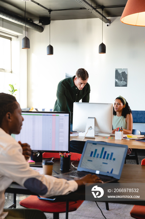 Caucasian young businessman discussing with biracial colleague over computer in office