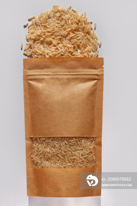 Kraft paper pouch bag with whole grain brown rice top view with harsh shadow on white background. Healthy diet food packaging mockup flat lay. Dry uncooked thai cereal high fiber magnesium antioxidant