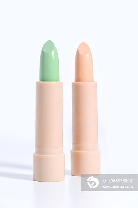 Foundation Green and beige face concealer isolated on white background. Preparing for face makeup. Two concealers in beige lids in the form of a lipstick. Skin color correcting concealers.