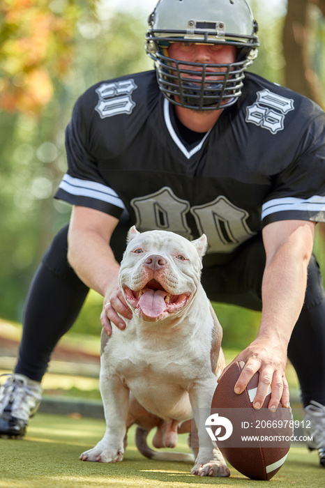 American football player with a dog posing on camera in a park. Copy space, sports banner. Concept american football, sport for the protection of animals.