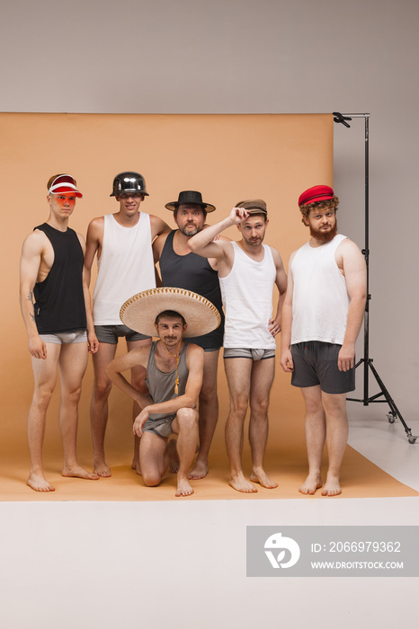 Diversity. Young cheerful people, men of different body types standing together in homewear and hats at studio photo shoot. Concept of art, fashion, friendship