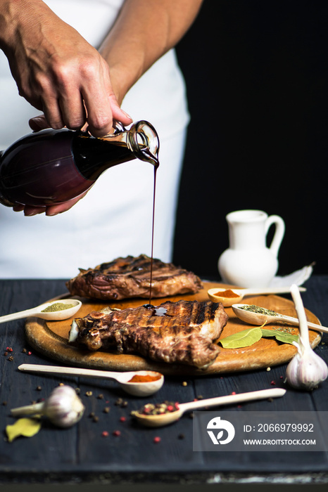 hand pouring pomegranate sauce to the appetizing barbecue pork meat with spices on a dark background