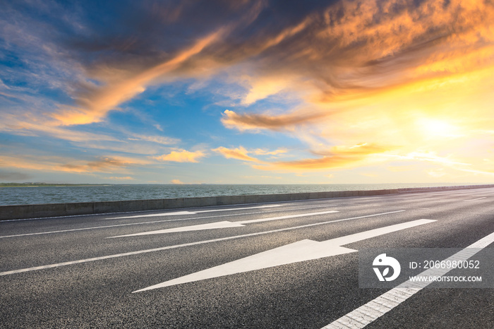 Asphalt road and dramatic sky with coastline at sunset