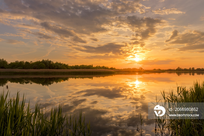 Sunset above the pond or lake with cloudy sky at summer and water reflection.