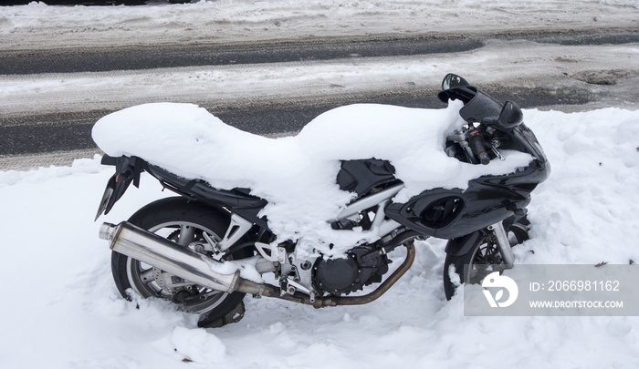 Snow covered motorcycle at the roadside of a snowy road