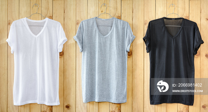 White T-shirt, Black T-shirt and Gray T-shirt hang on wood wall.