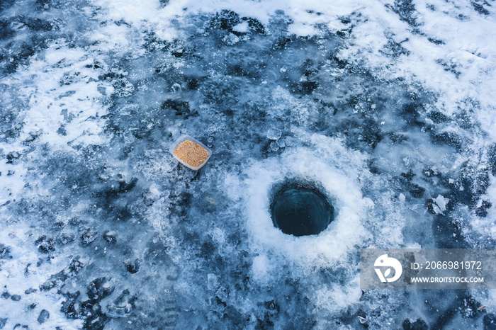 Ice fishing on a mountain lake. Fishing on the frozen surface of the lake. Frozen hole on ice.