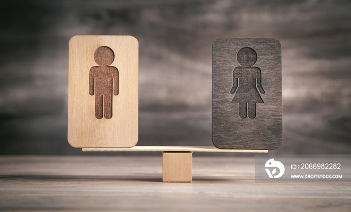 Male and female wooden symbols on balance scales.