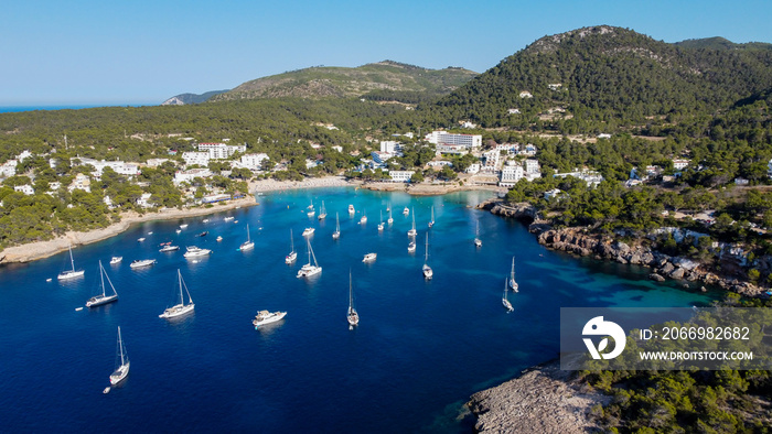 Aerial view of the bay of Portinatx on the north shore of Ibiza island in Spain - Yachts anchored near a sandy beach surrounded by pine forests and rocky cliffs in the Balearic Islands