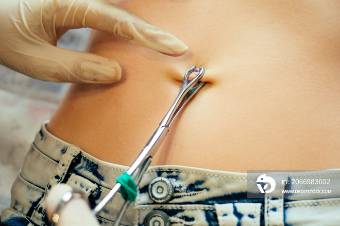 hand in a rubber glove close-up of master prepares to pierce the navel by belly of a young woman with a bandage and cotton on her stomach. care navel ring piercing concept