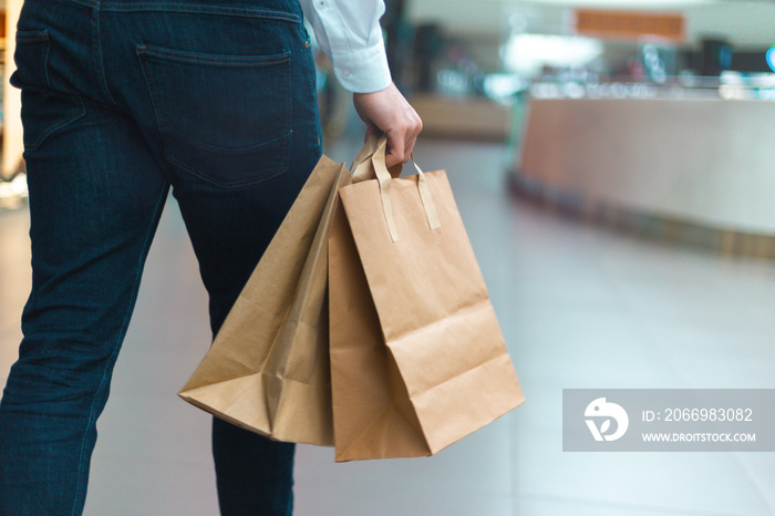 Closeup of a young stylish man walking in a mall with ecology friendly shopping bags in hand with goods and clothes. Sales, discount sold out concept. Seasonal sell out.