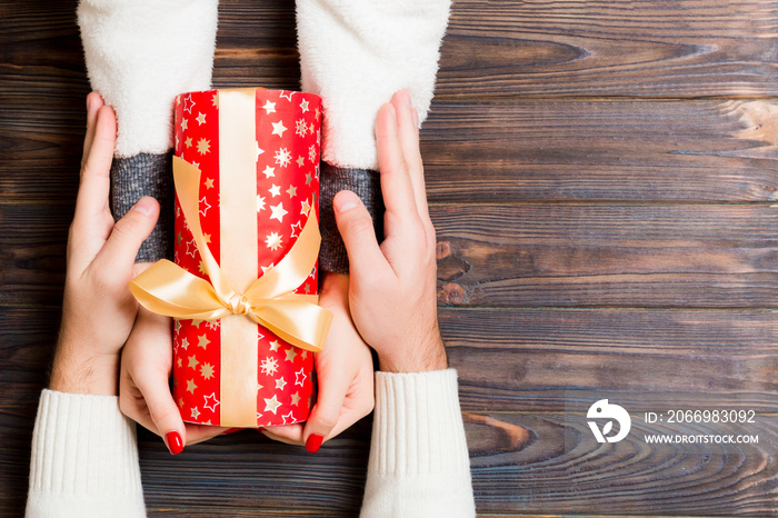 Top view of giving and receiving a present on wooden background. A man and a woman holding gift in hands. Festive concept with copy space