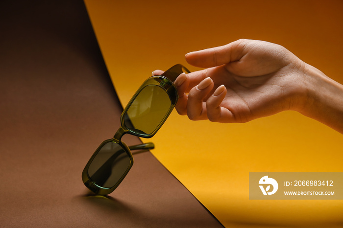 Female hand with stylish sunglasses on colorful background