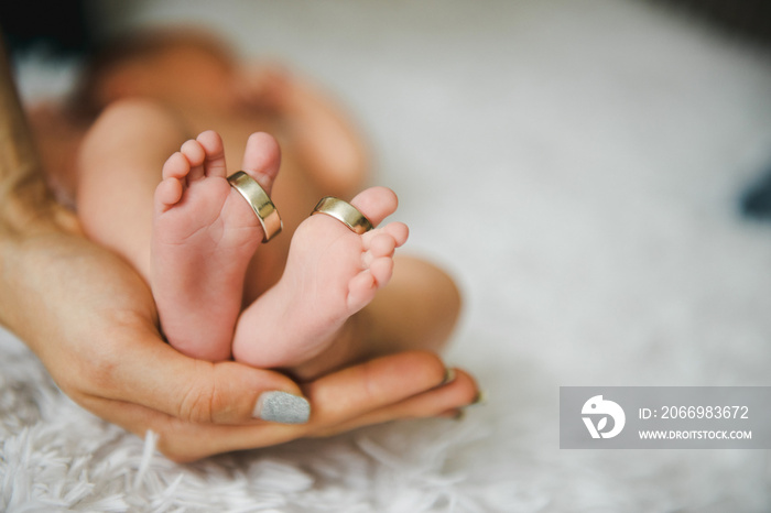 Close up baby feet with wedding rings on big toes. Mother hand hold feet. The concept of the family.