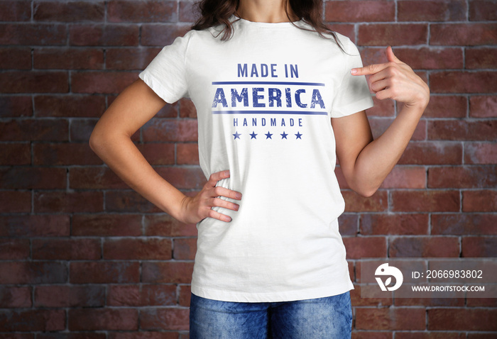 Woman in white t-shirt with text MADE IN AMERICA HANDMADE on brick wall background. Manufacturing quality concept.