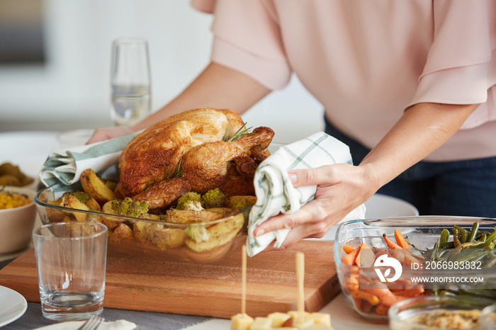 Close-up of woman putting the dish with roast turkey and potatoes on the dining table for Thanksgiving Day