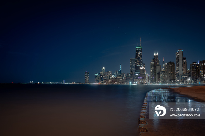 City of Chicago skyline night photograph with lights reflecting off of standing water washed up over the corrugated concrete shoreline along Lake Michigan in downtown.