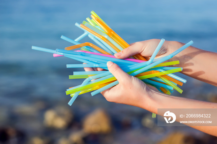 Close Up Of Hand Holding Plastic Straws Polluting Beach. Environmental pollution concept