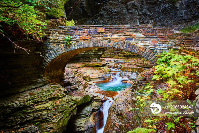 Beautiful stone arch walking bridge over gorge and river with blue waters and waterfalls during fall