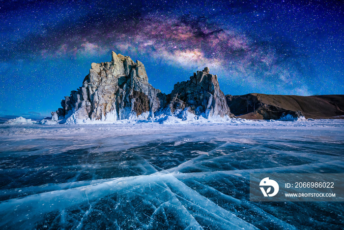 Landscape of Shamanka rock and milky way on sky with natural breaking ice in frozen water on Lake Baikal, Siberia, Russia.