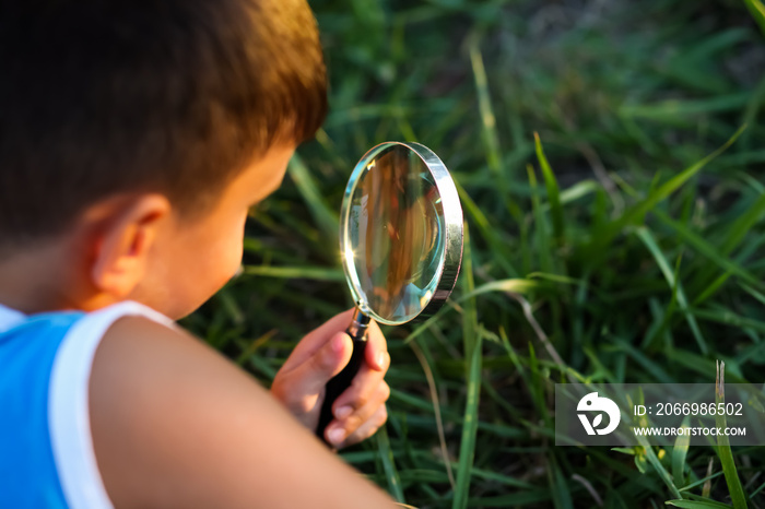 Cute little child boy looking through a magnifying glass on the tree in the garden. Study of plants.