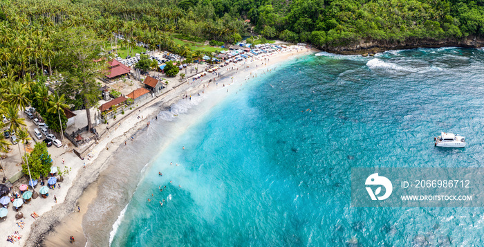 Magnificent aerial panorama up down photo of tropical beach at the end of mountain valley with coconut palms, boats in blue water, unrecognized tourists at Crystal Bay beach, Nusa Penida, Bali