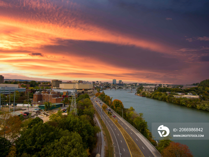 aerial shot along the green waters of the Tennessee River surrounded by building in the cityscape and autumn colored trees and lush green trees with powerful clouds at sunset in Knoxville Tennessee