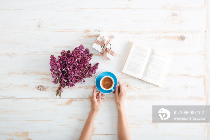 Hands of woman drinking coffee and reading book on table