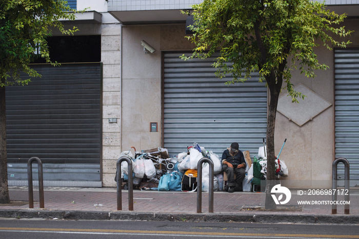 Male isolated homeless wearing a brown hat sitting on the pedestrian.