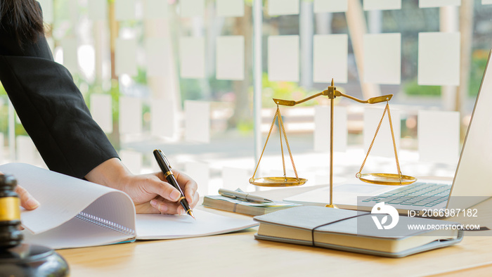 A female attorney looks at a contract document with a brass scale on a wooden table in the office. Law legal services concept of justice