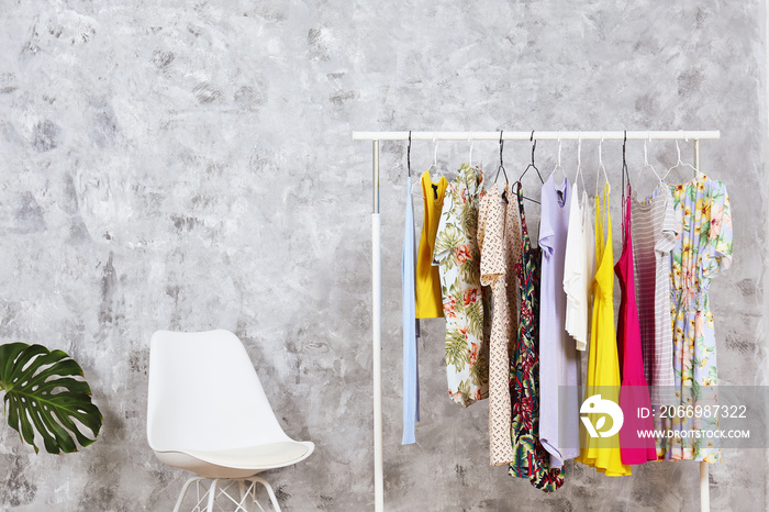 Women’s hip clothing store interior concept. Row of different colorful female clothes hanging on rack in hipster fashion show room in shopping mall. Grunged concrete wall background. Copy space.