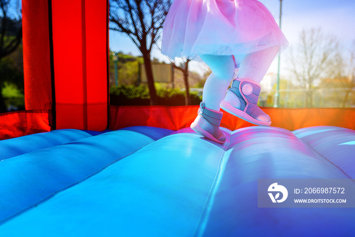 Close-up portrait of female joyful little girl legs jumps on a big inflatable trampoline outdoors in the park.