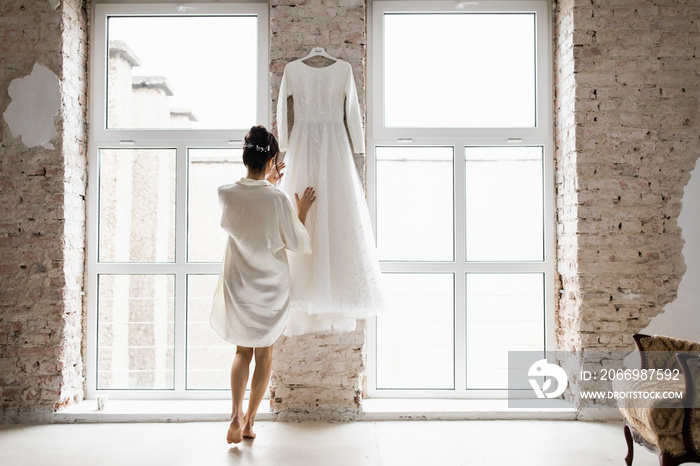 The bride at the big window is dressed in a man’s shirt.