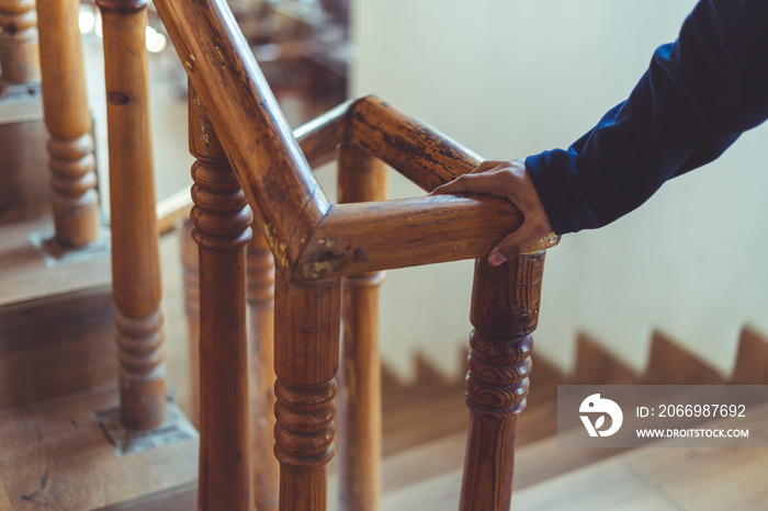 support, help and people concept- Close up of a man’s hand holding to a wooden railing while climbing a staircase.