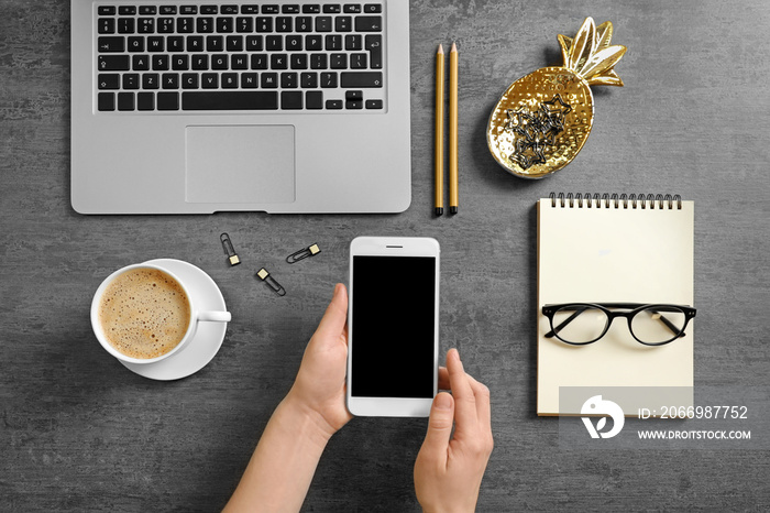 Woman holding phone over table with laptop. Mockup for design