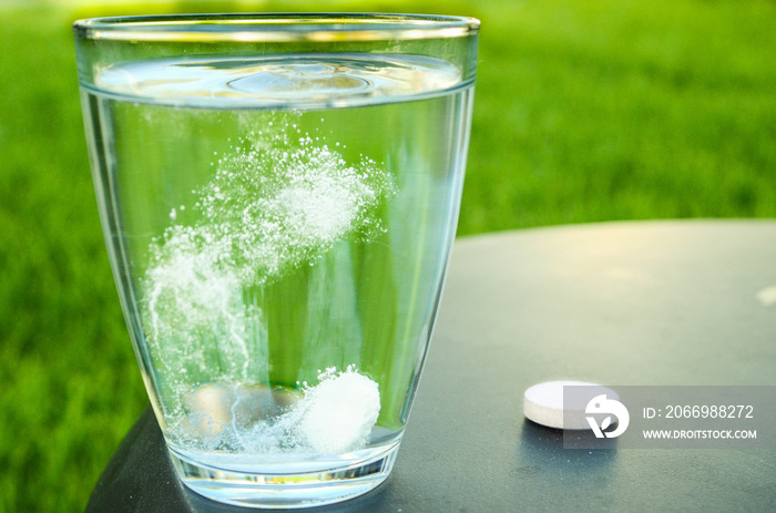 Effervescent Aspirine tablet in glass of water on black table - green grass background