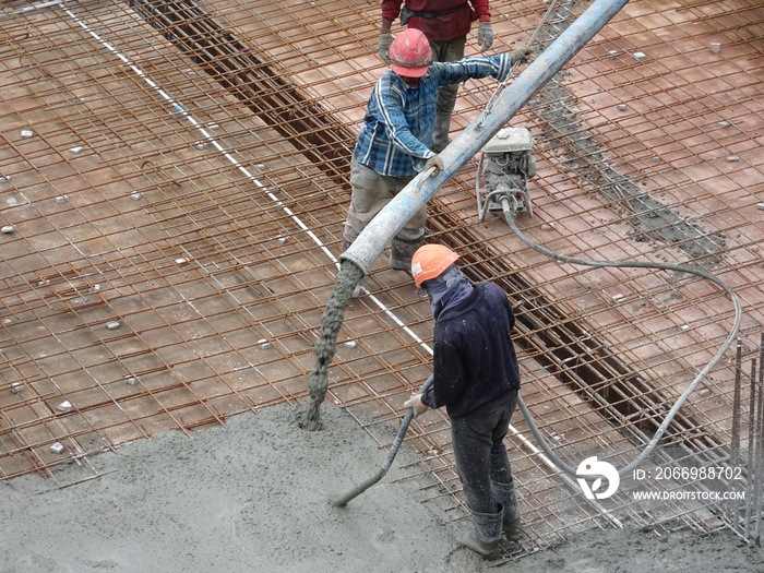 Construction workers pouring wet concrete using concrete spider hose from concrete pumping machine into floor slab form work at the construction site.