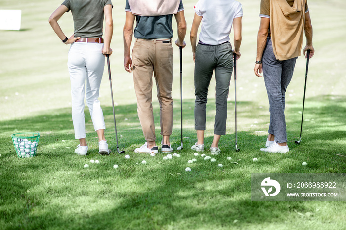 Friends standing together with golf equipment and balls on the green grass, cropped image with no face