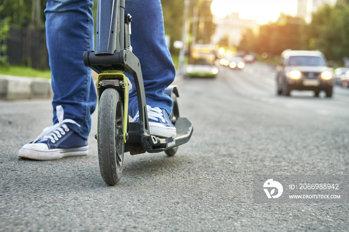 Female feet wearing gumshoes riding on kick scooter along busy street close up