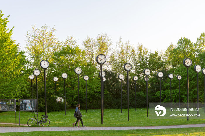 Zeitfeld, Installations art which are row of clocks on columns designed by Klaus Rinke, located in Volksgarten city park,  with view of sunny evening in the park.