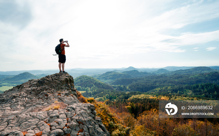 Outdoor young man with a water bottle at the edge of a cliff overlooking the mountains below. Drinking water from plastic bottle on rocky summit. Fantasy Adventure Composite