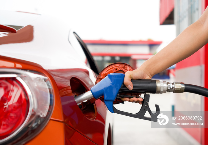 Gas station worker’s hand holding blue benzene gas pump, filling up red sport car tank. Close up