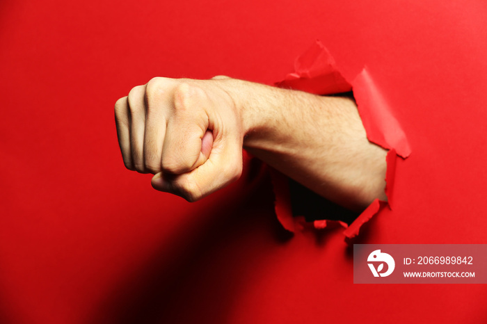 Male fist punching through red paper