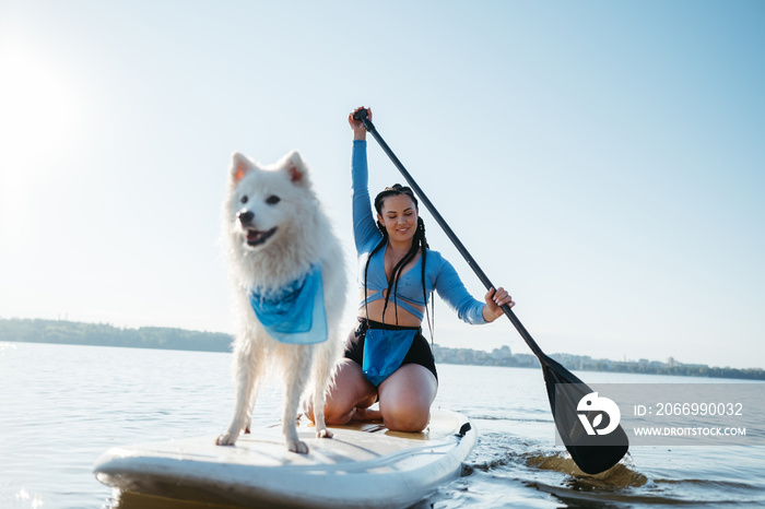 Cheerful Woman Paddleboarding with Her Pet on the City Lake, Snow-White Japanese Spitz Dog Standing on Sup Board