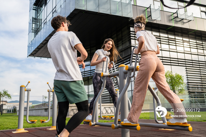 Group of friends man and women male and young adult people training at outdoor open gym in park in front of modern building real people sport and recreation exercise healthy lifestyle concept