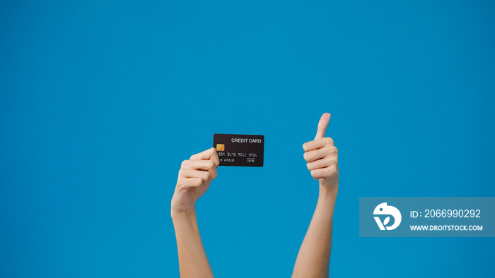 Young girl hold in hand credit bank card showing thumb up isolated over blue background in studio. Copy space for place a text, message for advertisement. Advertising area, mockup promotional content.