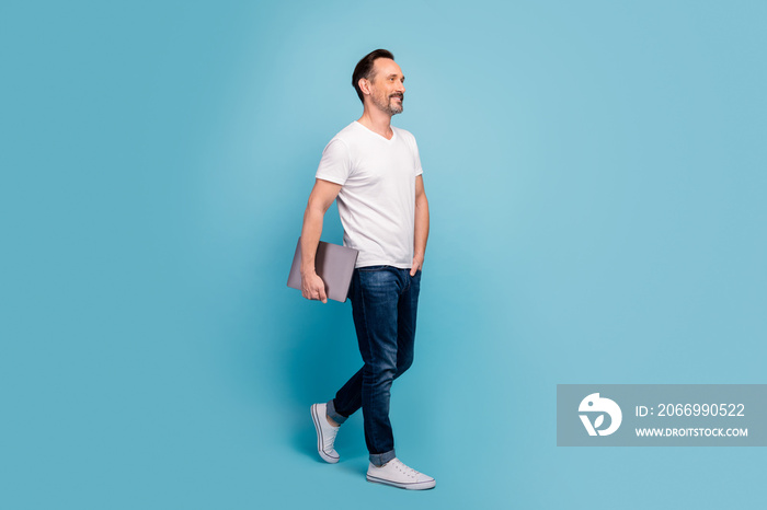 Full length body size view of his he nice attractive cheerful content mature guy walking carrying laptop isolated on bright vivid shine vibrant teal green blue turquoise color background