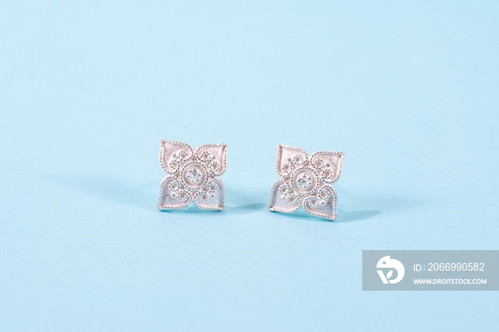 A pair of silver earrings on blue background.