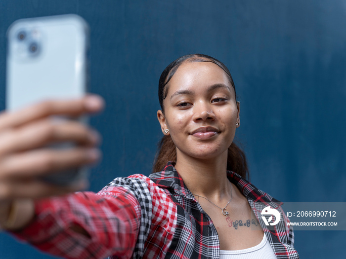 Young woman taking selfie against blue wall