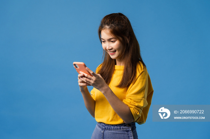 Young Asia lady using phone with positive expression, smiles broadly, dressed in casual clothing feeling happiness and standing isolated on blue background. Happy adorable glad woman rejoices success.